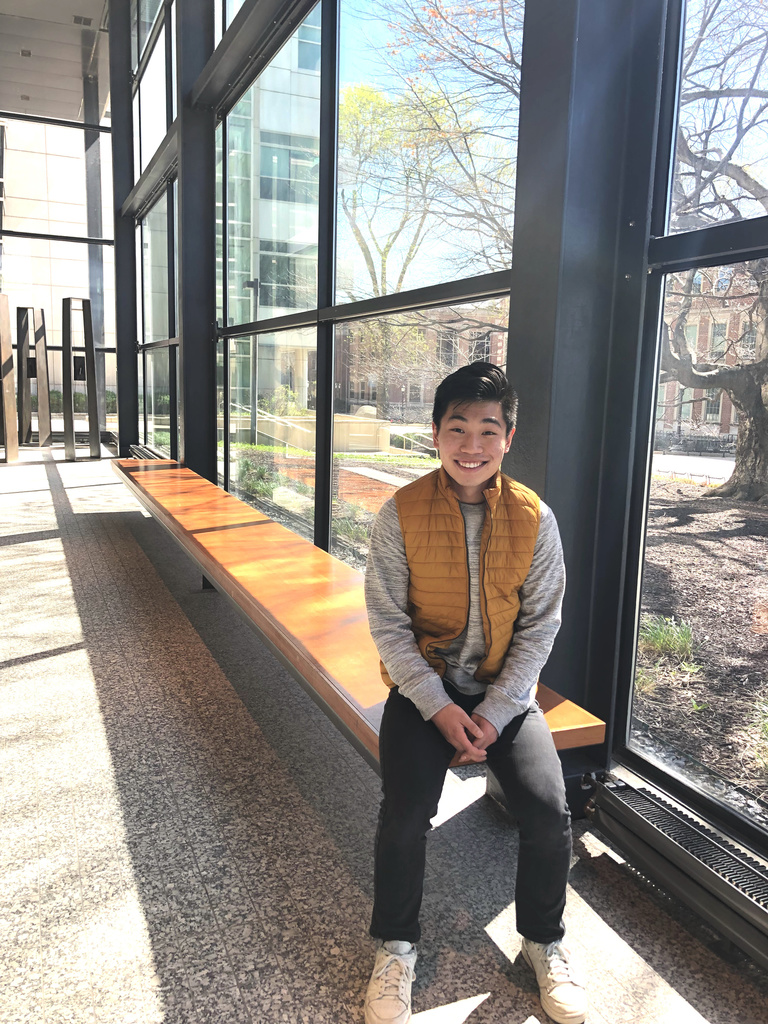 Young, Asian man sits on a bench in a sunny atrium
