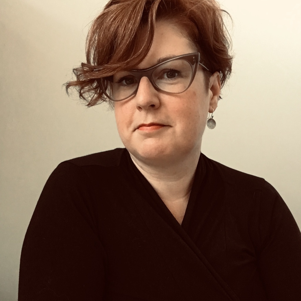 A white woman with read hair and gray glasses