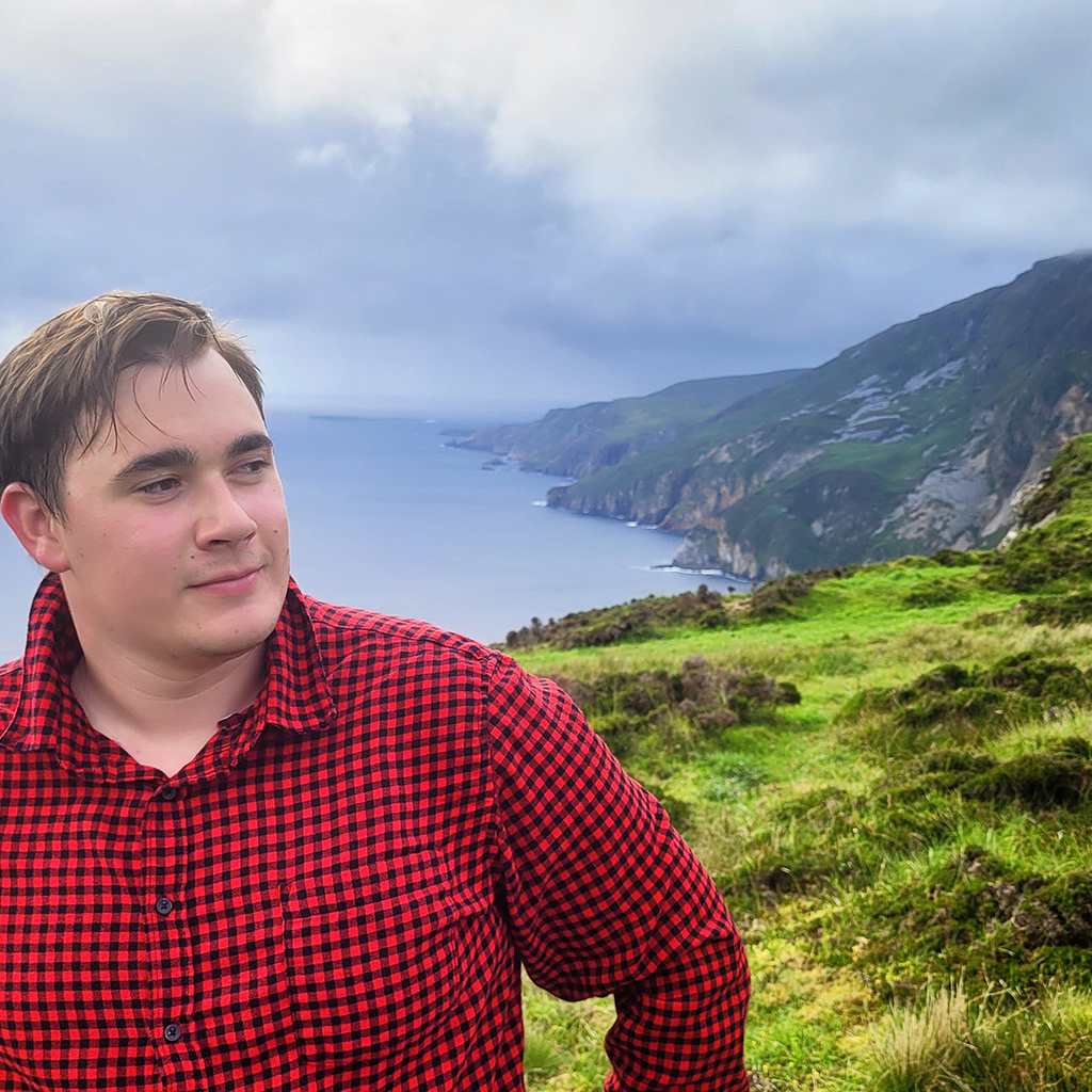 Young man in red and black flannel stands on a cliff