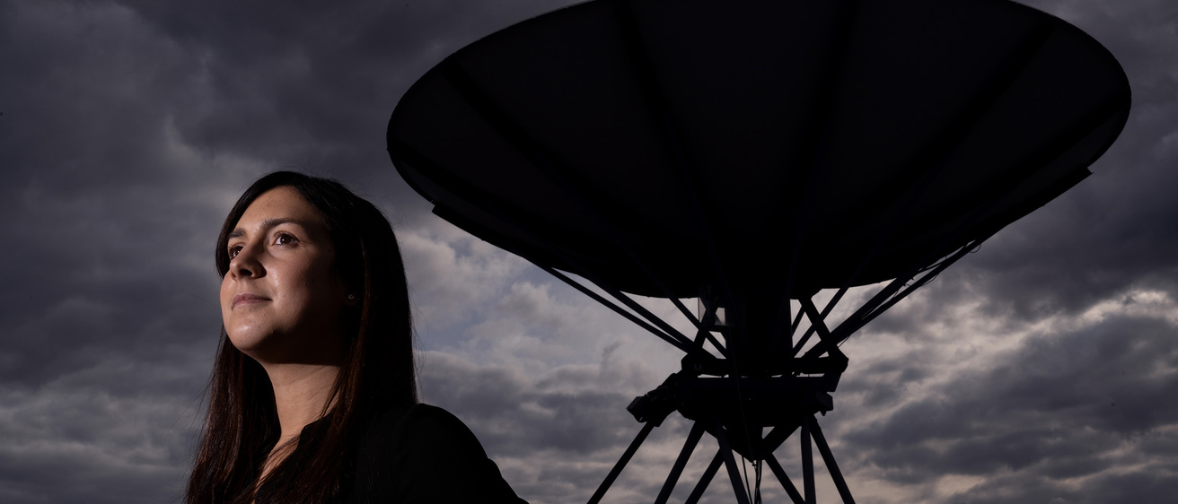 Woman looks out in the distance with a dark, cloudy sky and a satelite behind her