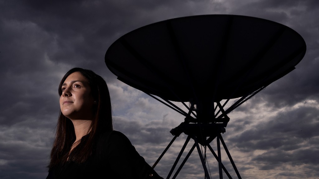 Woman looks out in the distance with a dark, cloudy sky and a satelite behind her